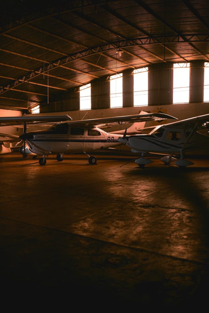 Two private airplanes parked inside a spacious, sunlit hangar with warm lighting.