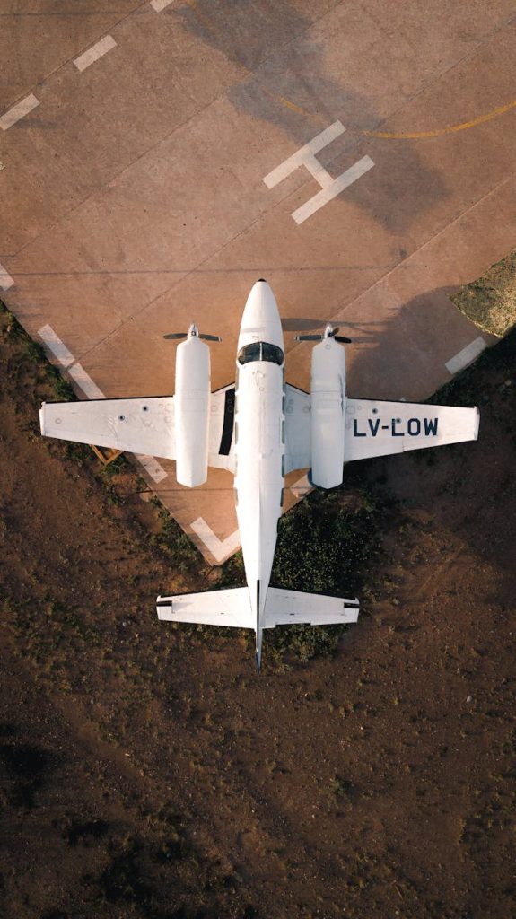 Aerial top view of white airplane with propellers on edge of paved airfield in light